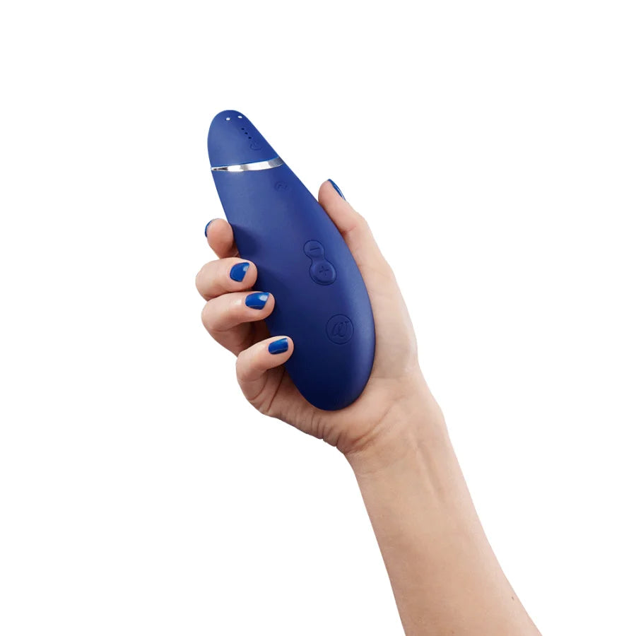 Womanizer Premium 2 held in hand, with power button, intensity buttons, and Womanizer logo visible.
